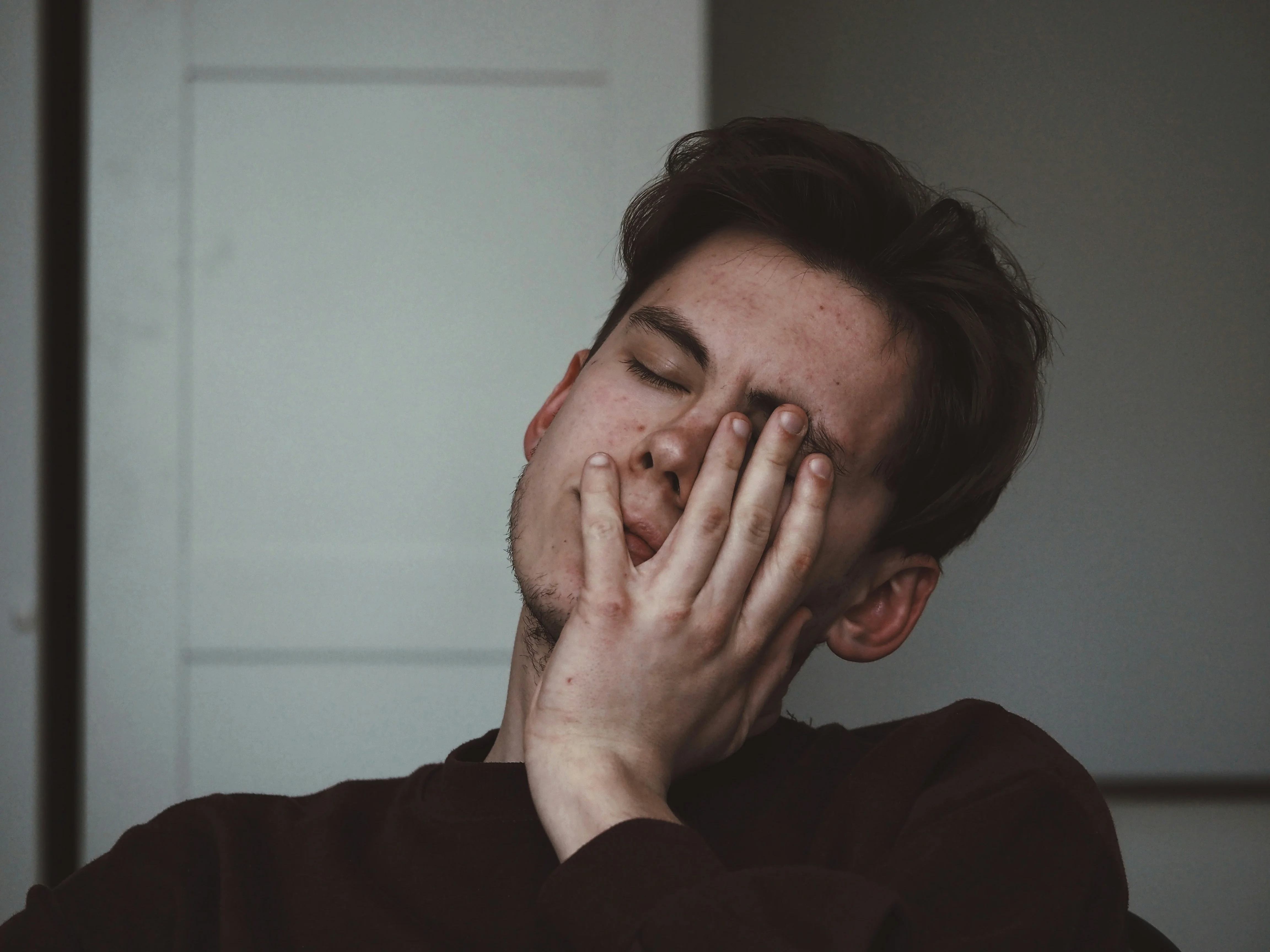 Mann mit geschlossenen Augen und einer Hand im Gesicht